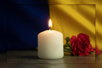 Fototapeta na wymiar One burning candle against the background of the national flag of Ukraine