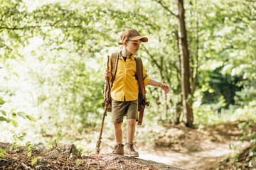 Boy traveler walking in the forest with rucksuck and stick