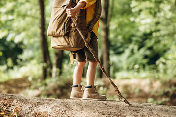 Boy traveler walking in the forest with rucksuck and stick