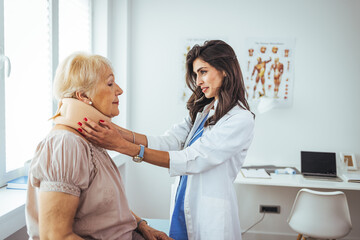 Female doctor putting neck orthopaedic collar on adult injured woman. Picture of senior woman...