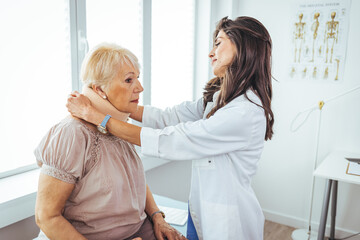 Obraz premium Doctor applying cervical collar on neck of senior woman in clinic. Female doctor putting neck orthopaedic collar on adult injured woman. Woman in pain at the doctor for a neck injury