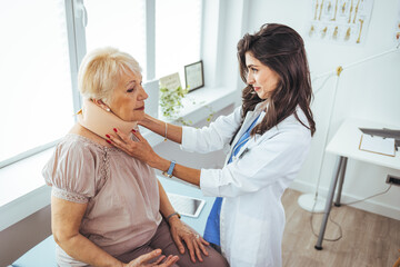 Young woman with injury of neck visiting doctor in clinic. Doctor examining a patient at desk in medical office. Doctor talking to a senior patient with cervical collar at the hospital