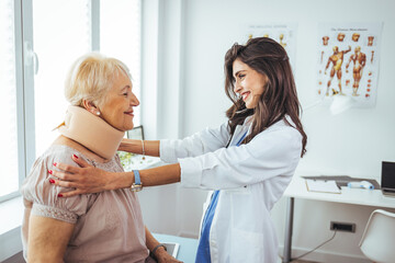 Female doctor putting neck orthopaedic collar on adult injured woman. Woman in pain at the doctor...