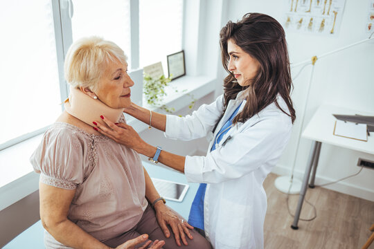 Doctor examining a senior female patient's x-ray, she is wearing a cervical collar and having a serious neck injury. Picture of adult woman having a visit at female doctor's office