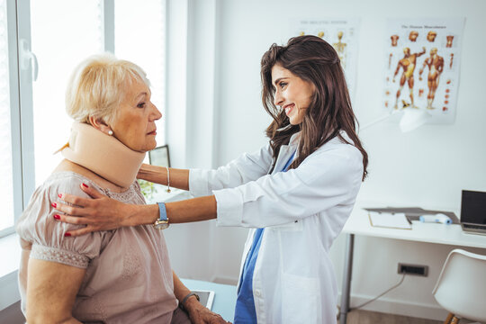 Female doctor putting neck orthopaedic collar on adult injured woman. Woman in pain at the doctor for a neck injury. Doctor giving a prescription to a senior patient with cervical collar