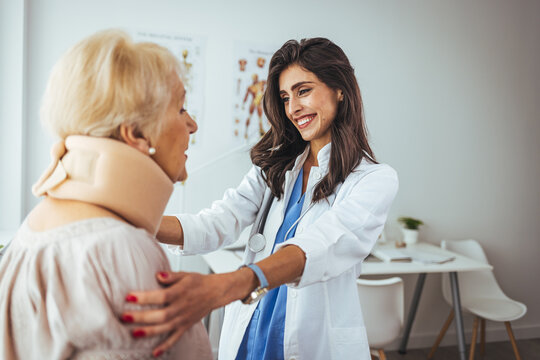 Young woman with injury of neck visiting doctor in clinic. Doctor examining a patient at desk in medical office. Doctor talking to a senior patient with cervical collar at the hospital