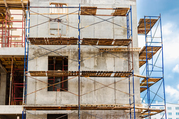 Construction of a new monolithic reinforced concrete house. Scaffolding on the facade of a building under construction. Working at height on a construction site.