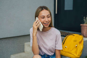 young adult female sitting in front steps of her home talking on mobile phone