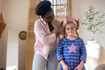Obraz premium African american woman putting a crown on head of a girl in blue dress