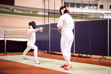 two fencers in white uniforms  are training to participate in a duel