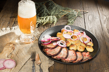 lunch of fried ham with potatoes and onions in a pan next to a glass of beer