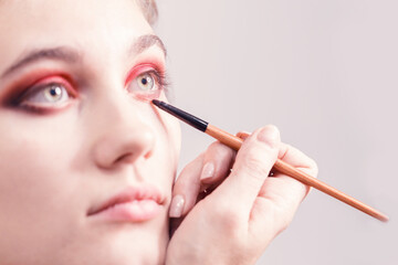 Makeup artist performs bright eye makeup. Eyeliner in red. Close-up.