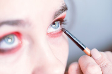 Obraz premium Performing eye makeup close-up. Bright red eyeshadow. Look up.