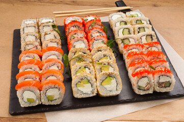 a large set of sushi rolls on a black stone plate