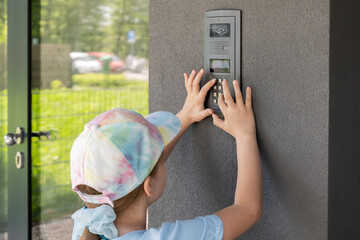 Elementary school age child, girl using a door entry phone, entering the entry code alone outdoors,...