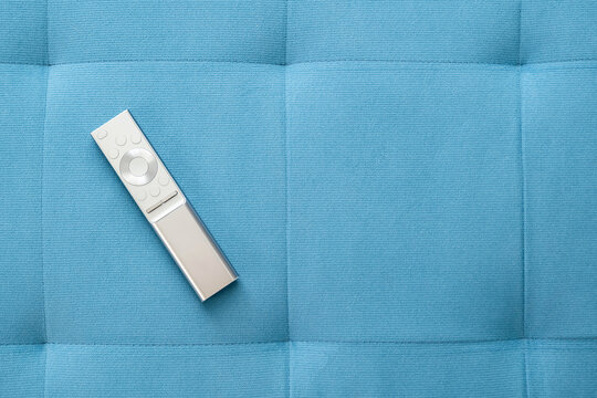 One Single Simple Sliver Smart TV Remote Control Laying On A Blue Sofa Pillow At Home, Object Top View, Closeup, Nobody. Leisure, Rest, Watching TV Symbol, Concept, Copy Space Background, No People