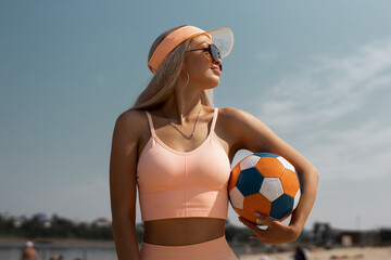 athletic young female in sunglasses on the beach in summer with a soccer ball