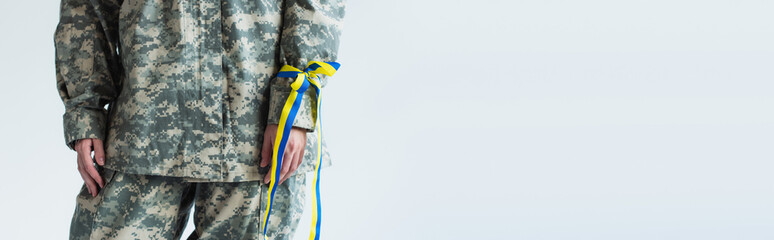 Cropped view of servicewoman in military uniform and blue and yellow ribbon on hand isolated on grey, banner