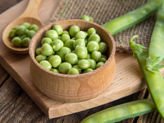 wooden bowl and spoon with fresh peas and their pods on an old wooden table, rustic background with peas