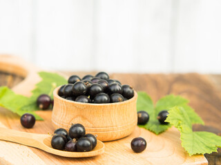 Fresh blackcurrant berries in a bowl on a wooden table near green leaves. Juicy natural currant fruits. Black currant