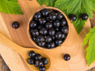 Fresh blackcurrant berries in a bowl on a wooden table near green leaves. Juicy natural currant fruits. Black currant