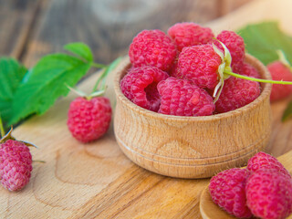 harvested red raspberries, large red garden raspberries in a wooden bowl on a wooden table