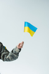 Cropped view of soldier in uniform holding ukrainian flag isolated on grey