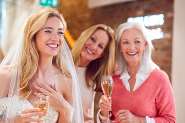 Grandmother With Mother Watching Adult Daughter Choosing And Trying On Wedding Dress In Bridal Store