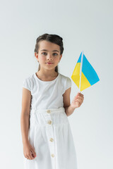 Girl holding ukrainian flag and looking at camera isolated on grey