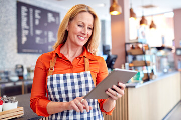Mature Female Owner Of Coffee Shop Or Restaurant Using Digital Tablet