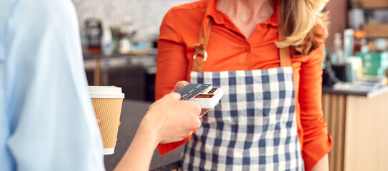 Close Up Of Female Customer In Coffee Shop Making Contactless Payment With Card