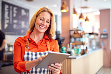 Mature Female Owner Of Coffee Shop Or Restaurant Using Digital Tablet