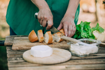 Stylish woman in green shirt make a snack with bread and cheese on a table in outdoor