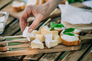 Stylish woman in green shirt make a snack with bread and cheese on a table in outdoor