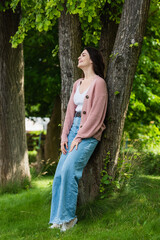 brunette woman in jeans smiling near trees in park