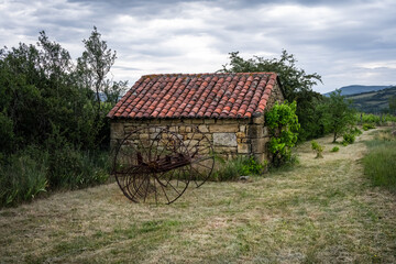 Stone hut and old hay rake in a field on a cloudy spring day, Auvergne, France