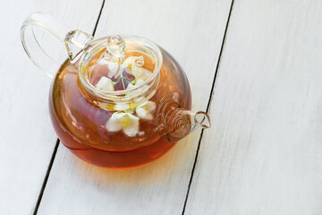Jasmine tea and flowers in glass teapot on a wooden white background, close up. Teapot with green jasmine tea