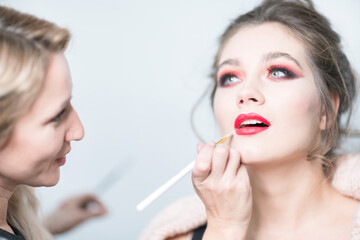 Obraz na płótnie Canvas Makeup artist applies red lipstick. Beautiful female face. Close-up.