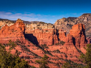 Gorgeous view of tall red rocks surrounded by dark green grass and trees under a clear bright sky