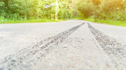 Car wheels traces on empty asphalt road at countryside closeup. Track through green summer forest. Travelling by auto. Old way at forestry site © MIKHAIL
