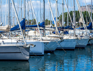 boats and yachts on pier in marine city port with masts and bulidings and blue sky on background