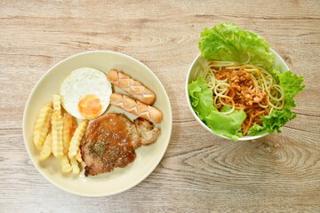 grilled pork steak dressing gravy sauce with french fries and fried egg couple sausage on plate and spaghetti dressing fried chop pork and slice tomato in ketchup sauce with vegetableon in bowl