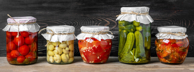 Homemade pickled cherry tomatoes, cucumbers, champignons, garlic, eggplant, red peppers in jars on wooden shelf Homemade canned and fermented foods concept Seasonal product - obrazy, fototapety, plakaty