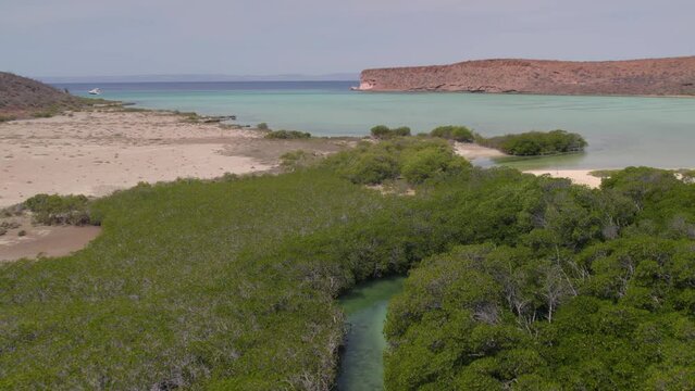 Aerial view of the wavy sea and the rocky mountains gleaming under the cloudy blue sky in 4K