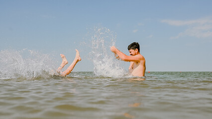Dad swims with his son in the sea. The father throws his son in the water. The boy does a somersault in the sea. The family spends their summer vacation at the sea.