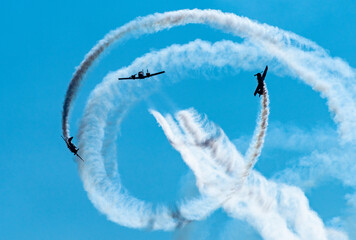 Silhouettes of training aircraft performing aerobatics on a clear sunny day. - obrazy, fototapety, plakaty
