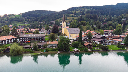 Typical Bavarian town church seen from Schliersee lake in drone view aerial footage