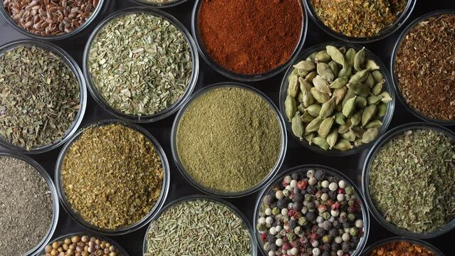 Assortment of aromatic spices, seeds and dry herbs for cooking food on background rotating in smal glass bowls rotating, close up, top view