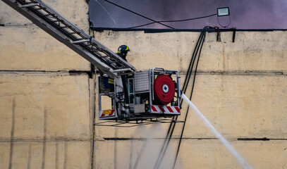 The fire brigade, standing on the fire escape, extinguishes a fire in an industrial building with a...