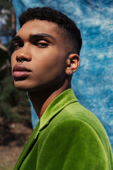 portrait of african american man with piercing looking at camera near blue cloth on blurred background